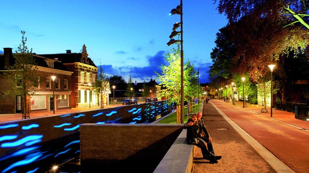 People are sitting next to the canal, enjoying the nicely lit area