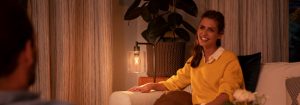 "Cozy living room ambiance created by warm LED table lamp, illuminating woman in yellow sweater enjoying evening conversation."